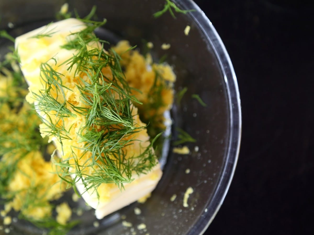 Eine Glasschüssel mit Zitronen-Dill-Butter auf einem dunklen Tisch.