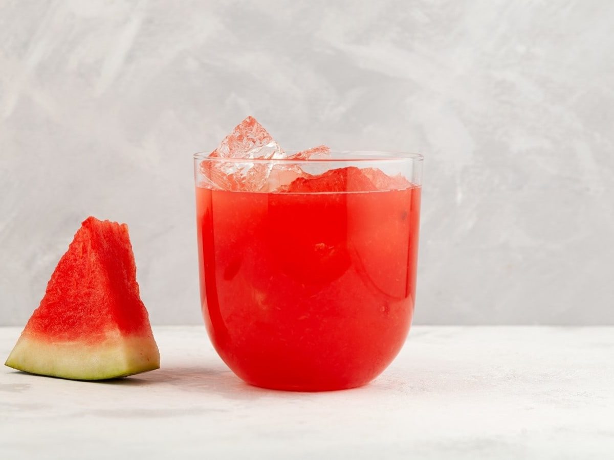 Ein Glas Agua fresca neben einem Stück Wassermelone.