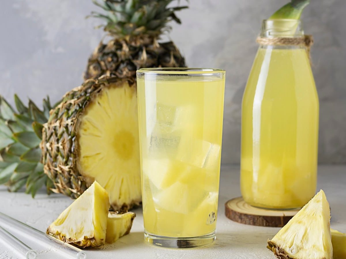 Ein Glas mit Ananas-Eistee vor einer frischen Ananas.