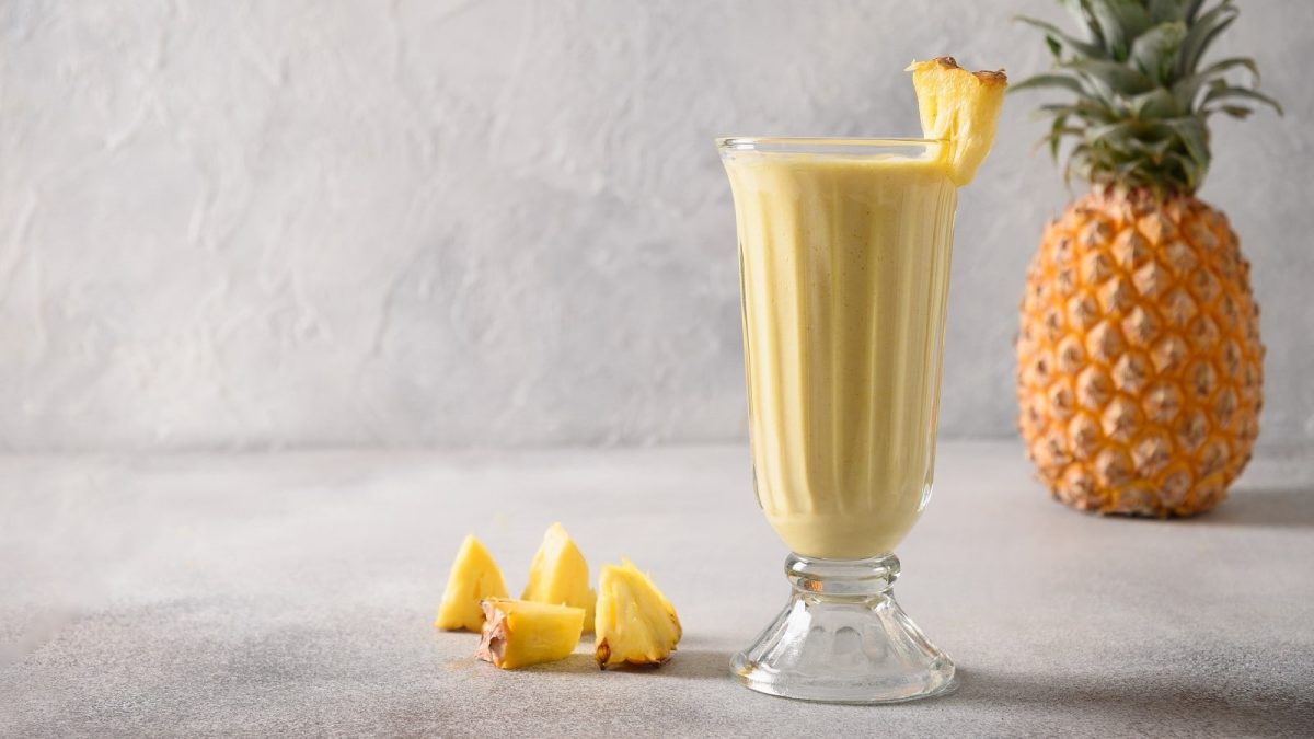 Ein Glas Ananas-Lassi vor einer frischen Ananas.