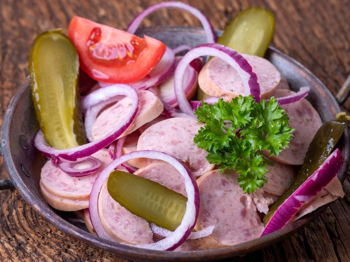 Draufsicht: eine Schüssel bayerischer Wurstsalat steht auf einem Tisch aus Holz.