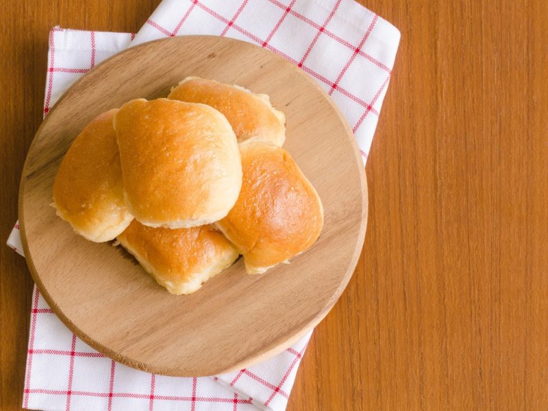 Das beste Brötchen zum Grillen vier Brötchen gestapelt auf einem Holzbrett, Tuch und hellem Untergrund. Draufsicht.