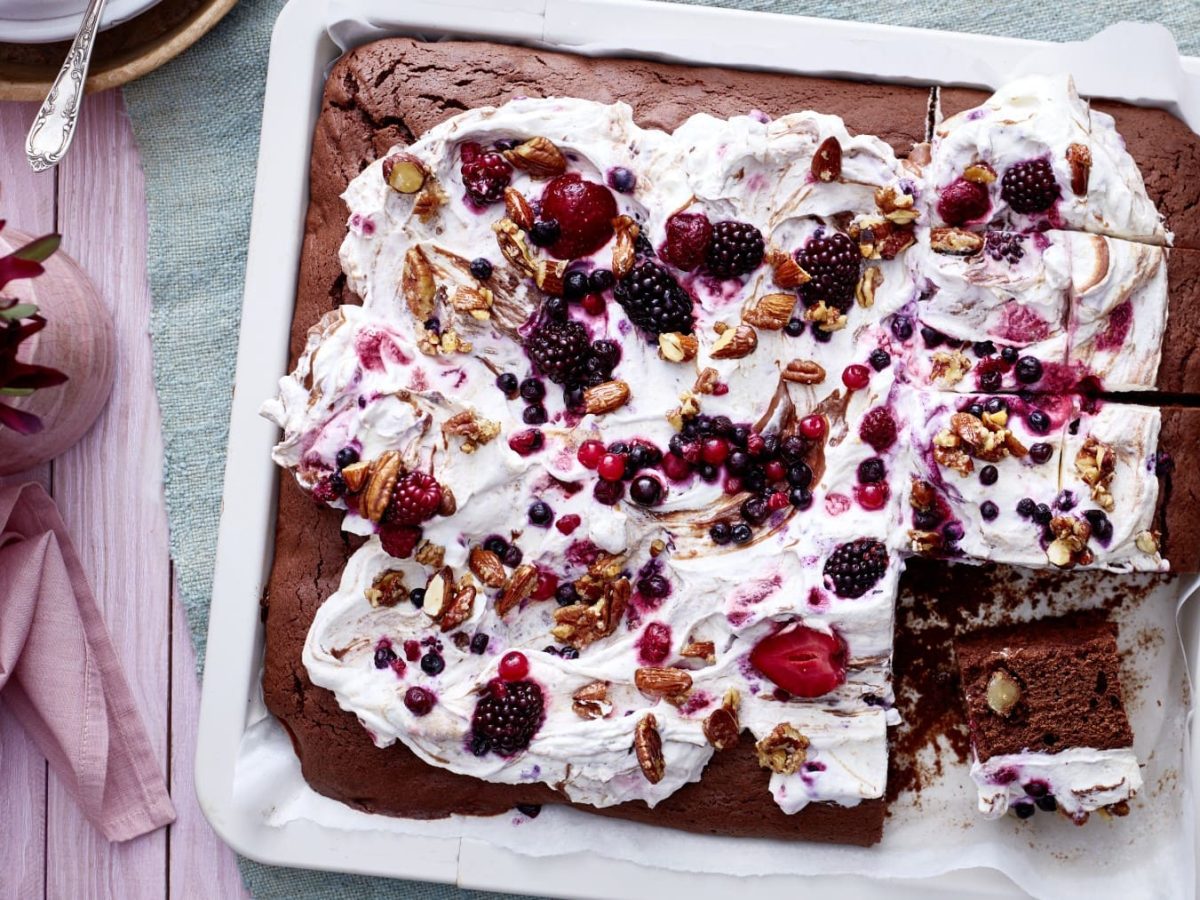 Ein weißes Blech mit Brownies auf einem hellblauen Geschirrtuch auf einem rosa Untergrund. Links davon eine kleine Pflanze.