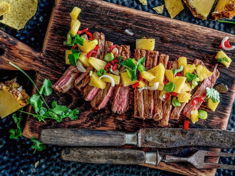 Carne Asada, gegrilltes Steak mit Ananas, in Scheiben geschnitten und auf einem Holzbrett angerichtet, daneben Nacho-Chips.