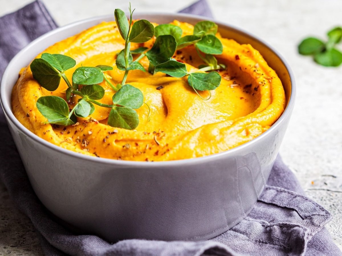 Eine graue Schale mit dem Mandel-Curry-Dip und Kresse auf einem grauen Tisch mit grau-blauem Küchentuch.