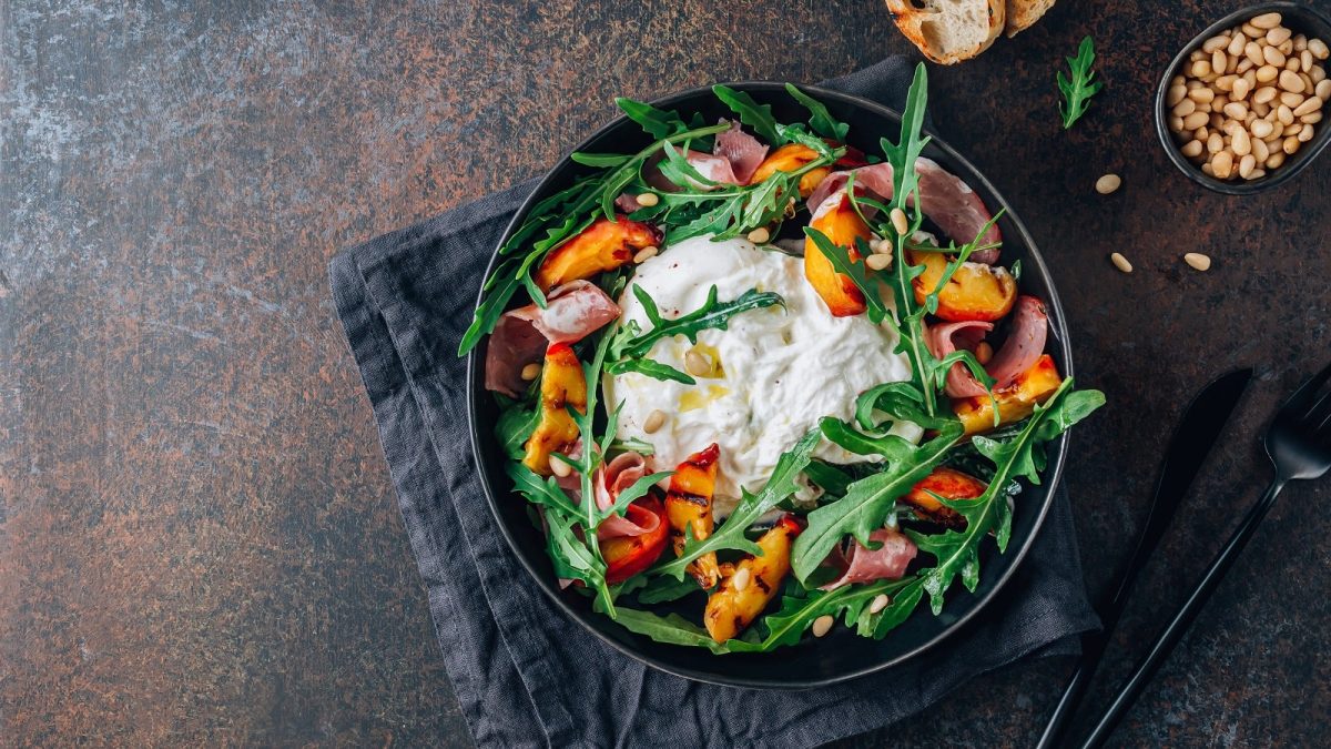 Ein Teller mit Rucola-Salat mit gegrilltem Pfirsich auf einem dunklen Tisch.