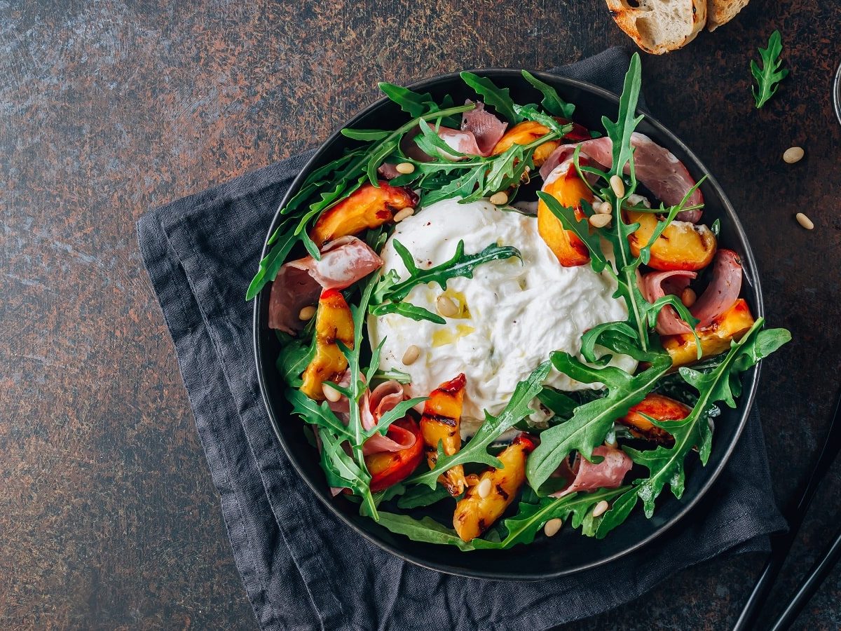 Ein Teller mit Rucola-Salat mit gegrilltem Pfirsich auf einem dunklen Tisch.