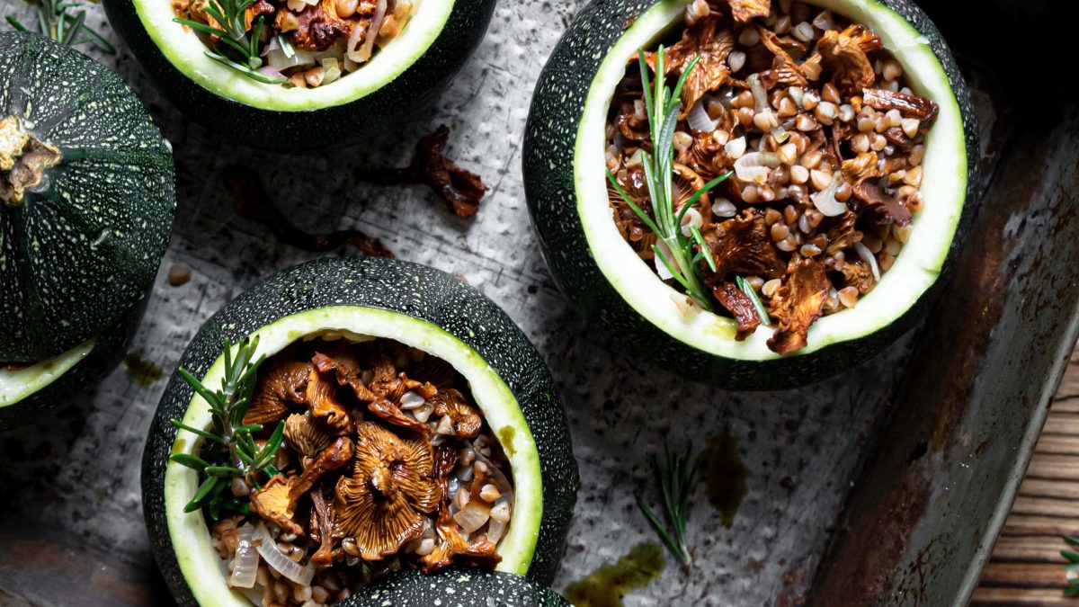 Draufsicht: drei runde gefüllte Zucchini mit Pfifferlingen stehen auf einem Untergrund aus Holz.