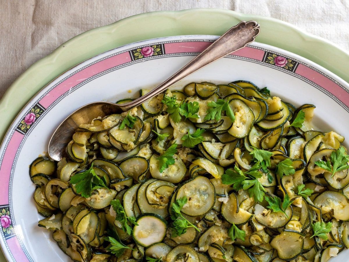 Ein Teller geschmorte Zucchini mit Zimt, Sardellen und Knoblauch, darin ein Löffel.