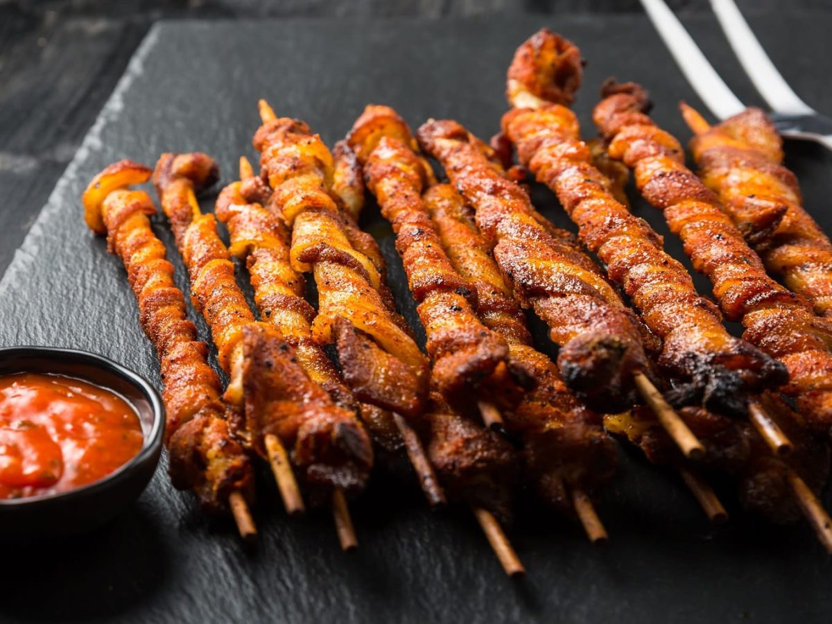 Einige Grillfackeln auf einer schwarzen Schieferplatte mit einem kleinen Schälchen roter Sauce.