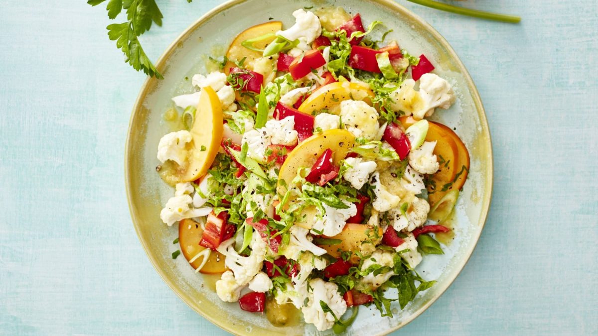 Draufsicht: Healthy Blumenkohl-Bowl auf einem Teller mit hellblauem Untergrund, über dem Teller am Bildrand ein Stiel Petersilie.