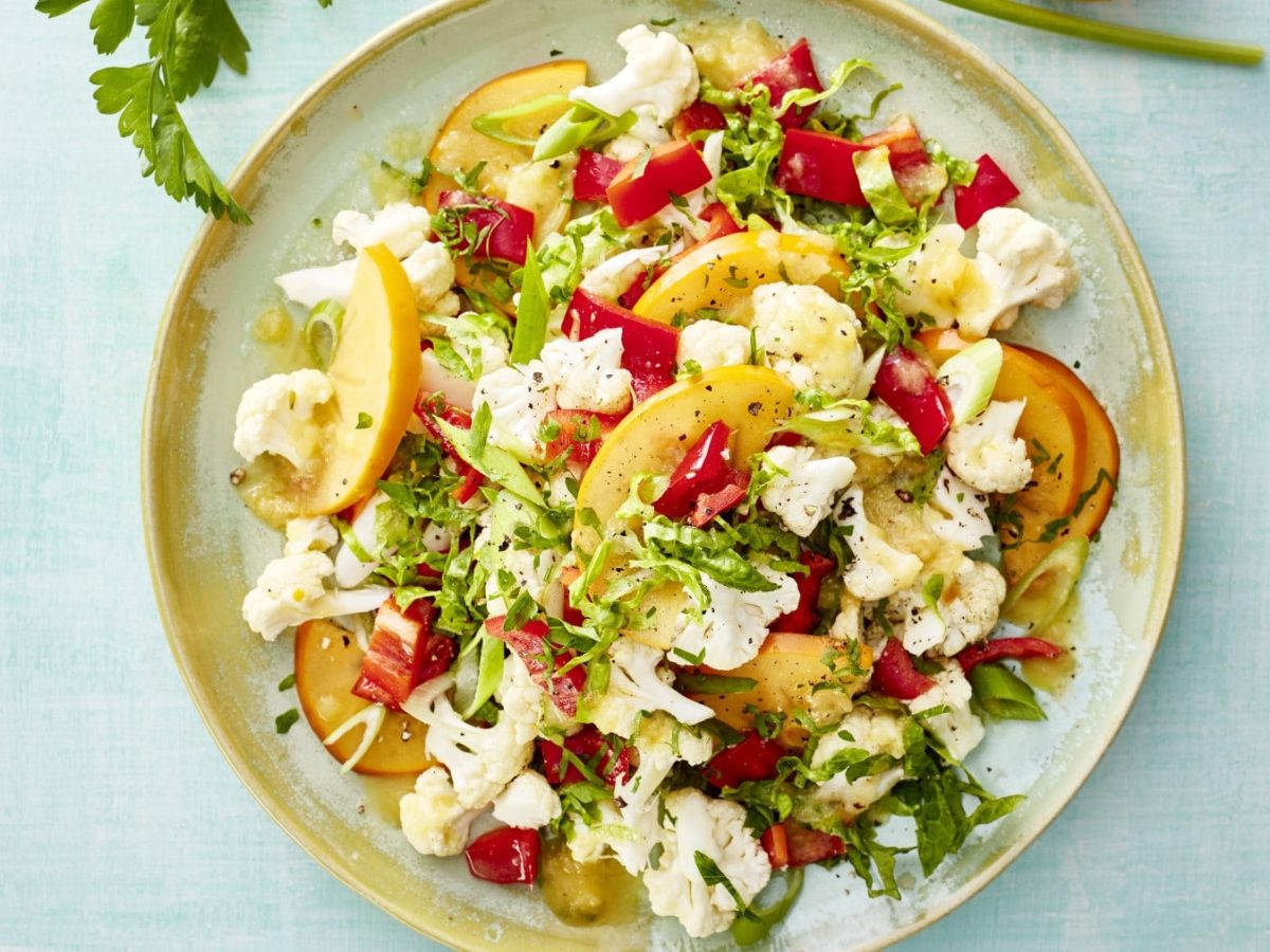 Draufsicht: Healthy Blumenkohl-Bowl auf einem Teller mit hellblauem Untergrund, über dem Teller am Bildrand ein Stiel Petersilie.