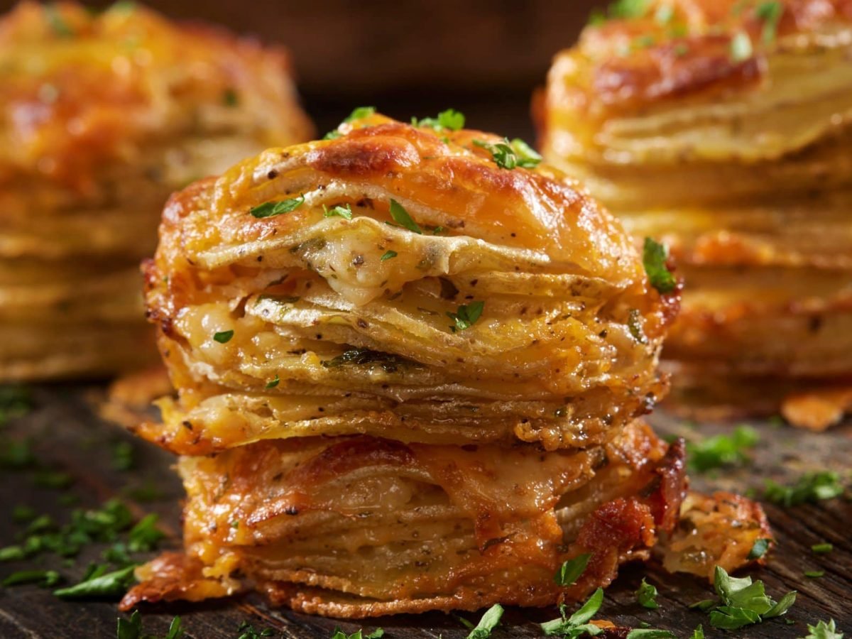 Kartoffelstapel mit Gruyère bestreut mit Petersilie auf Holzplatte.