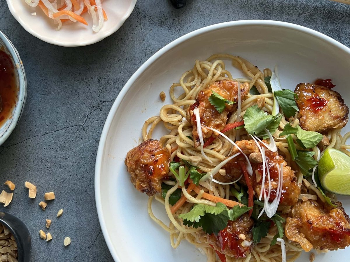 Kochboxen getestet killbillbao Popcorn Chicken mit asiatischem Nudelsalat auf weißem Teller. Pickles, Sauce und Erdnüsse in weißen Schalen im Bild auf grauem Untergrund. raufsicht.