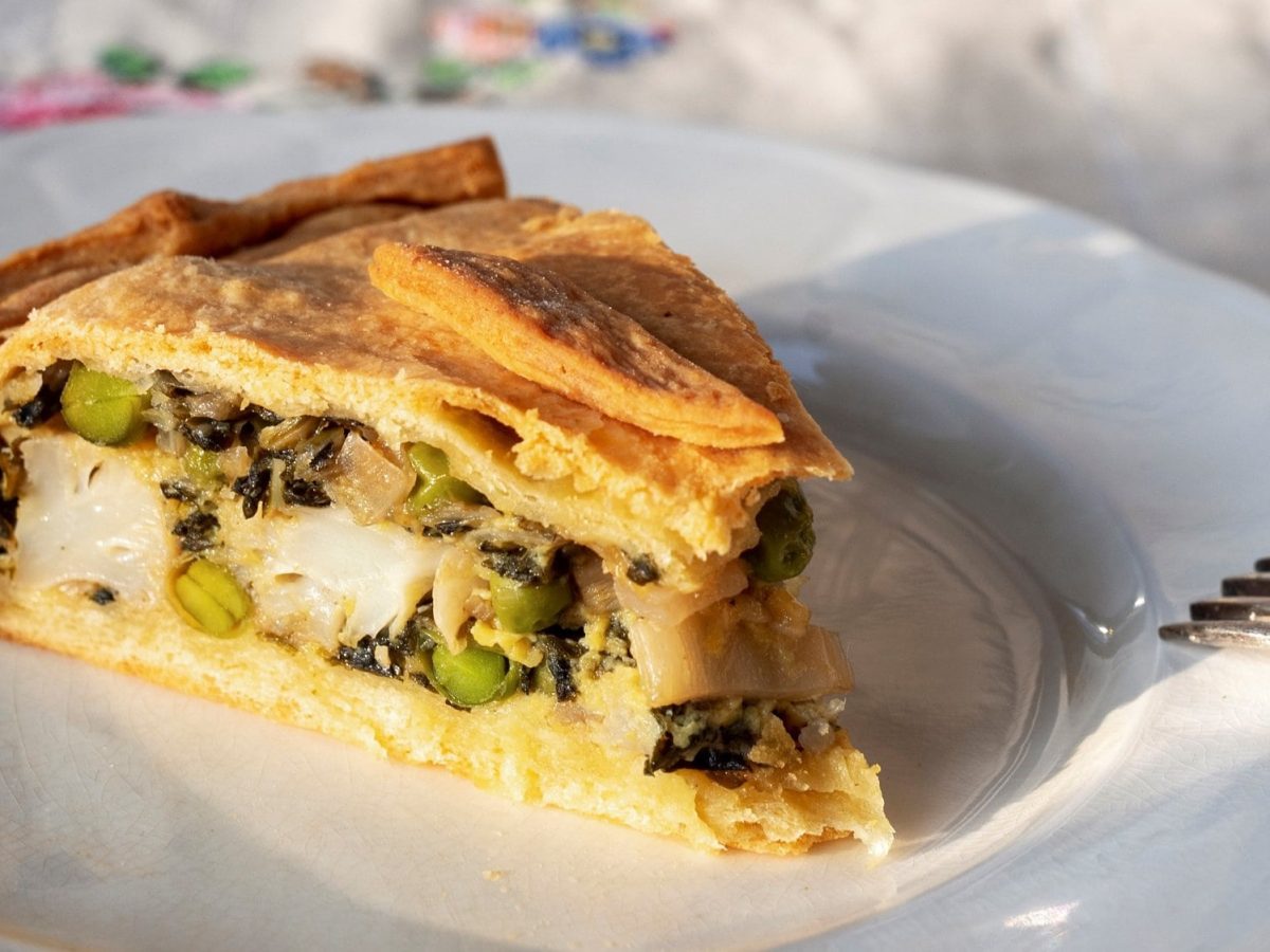 Ein Stück kroatische Mangold-Blumenkohl-Tarte auf einem Teller, daneben eine Gabel.