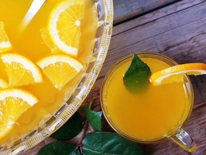 Eine große Glasschale mit dem gelben Punsch und daneben einem kleinen Glas mit dem Lillet Passion Punsch auf einem dunklen Holztisch.