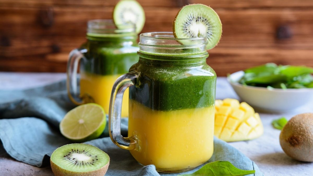 Zwei Gläser mit Mango-Kiwi-Smoothie auf einer blauen Decke.