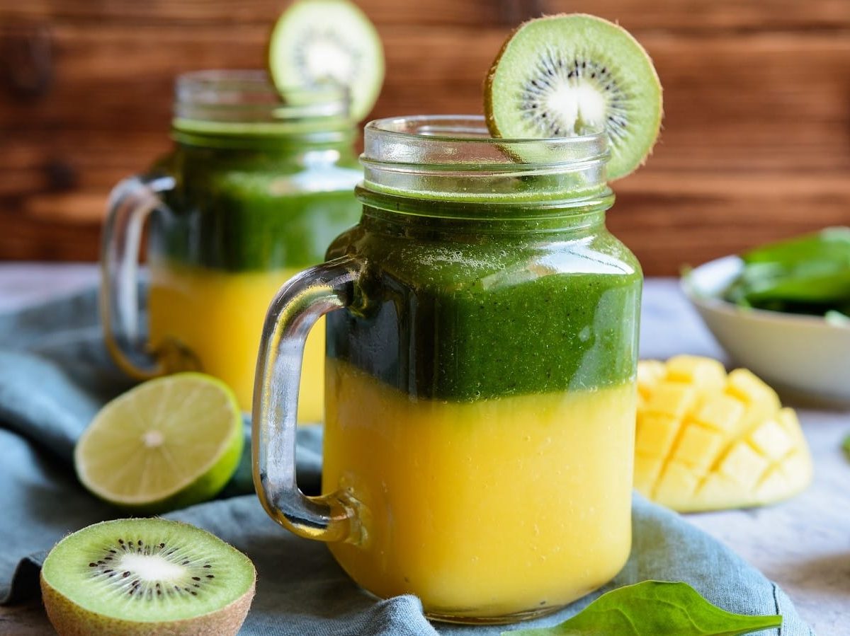 Zwei Gläser mit Mango-Kiwi-Smoothie auf einer blauen Decke.