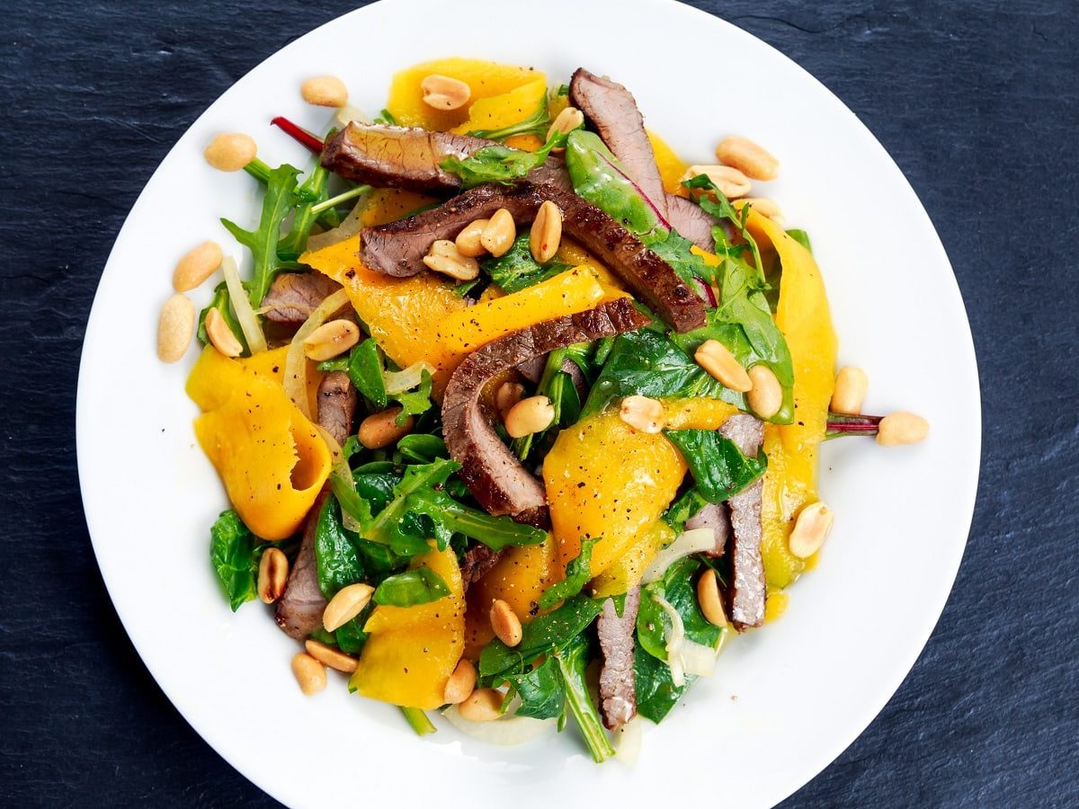 Ein weißer Teller mit Mangosalat mit Rind auf einem dunklen Tisch.