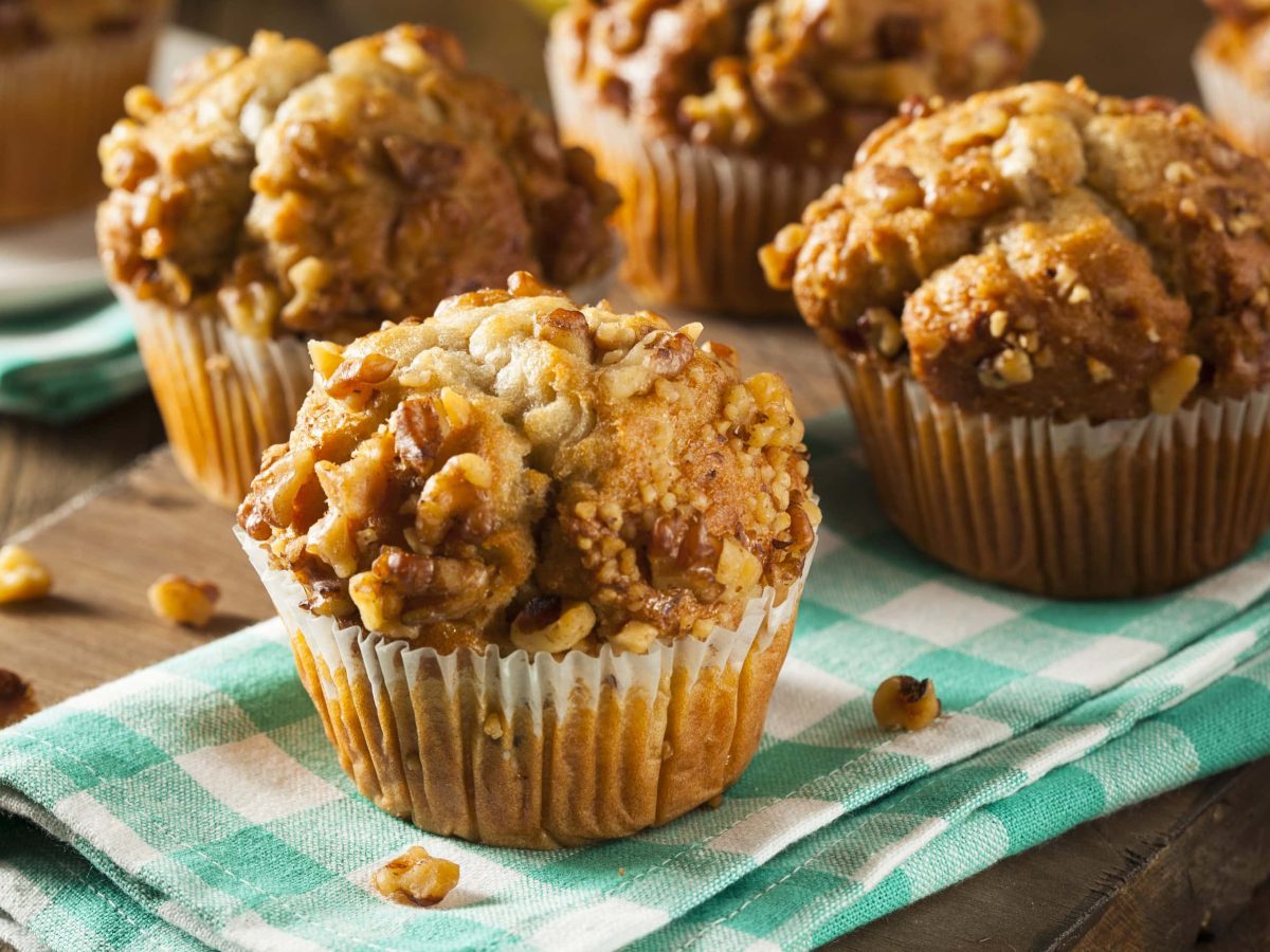 Mehrere Muffins auf einem dunklen Holztisch mit grün-weiß-karierter Tischdecke.