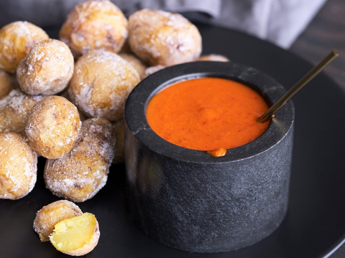 Ein schwarzer Teller mit Papas Arrugadas und dem rötlichen Dip Mojo rojo auf dunklem Holztisch.