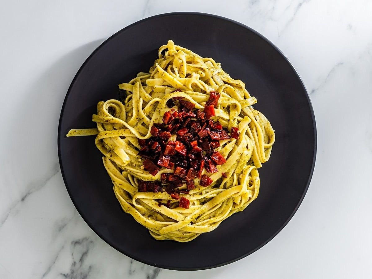 Pasta mit Rotebetespeck auf einem schwarzen Teller.