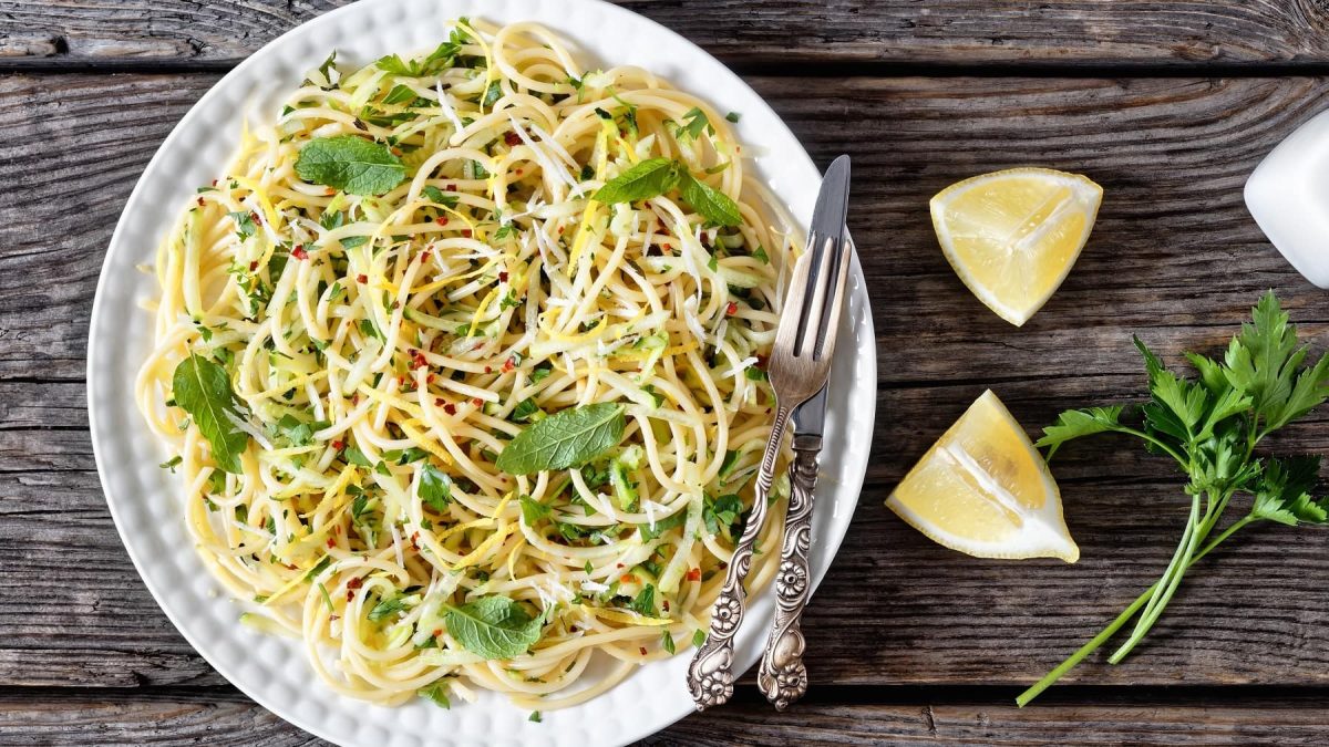 Ein weißer Teller mit der Pasta auf einem dunklen, rustikalem Holztisch. Neben der Spaghetti Carrettiera liegen Zitronenecken und Petersilie.