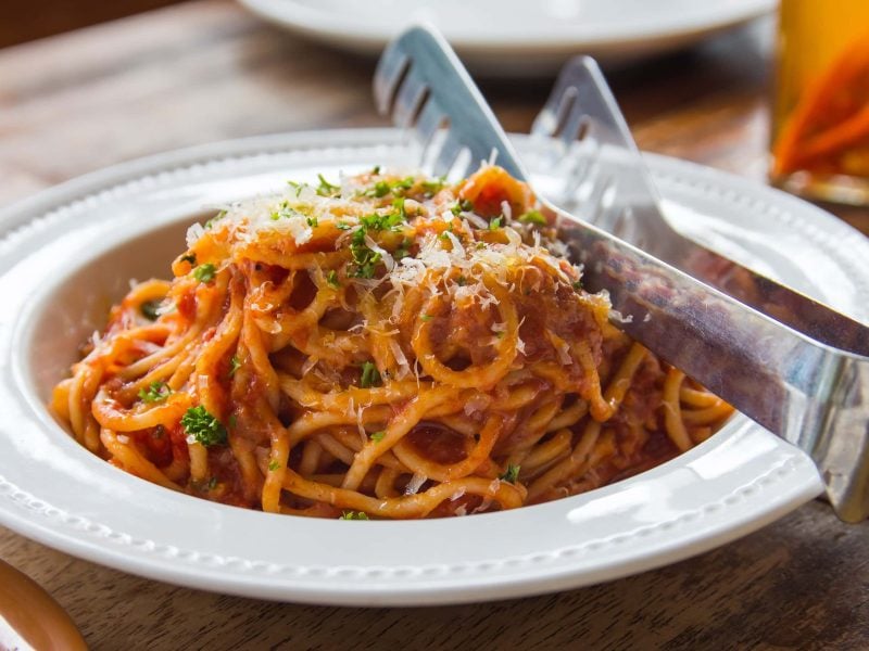 Thunfisch-Bolognese bestreut mit Parmesan und frischer Petersilie auf weißem Teller mit einer Nudelzange.