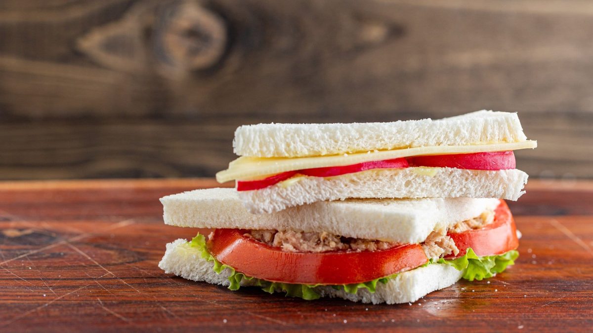 Ein Tramezzini mit Tomate und Thunfisch liegt auf einem lackierten Untergrund aus Holz.