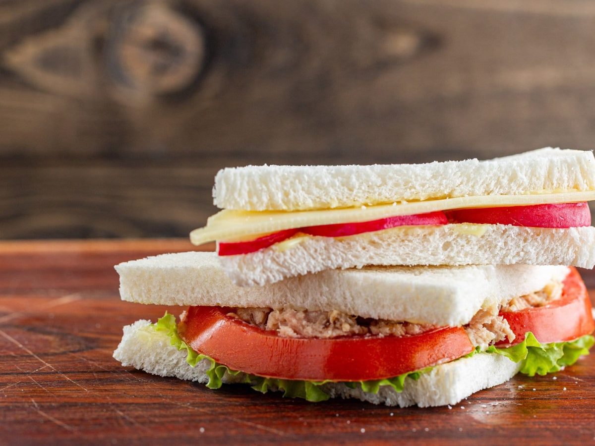 Ein Tramezzini mit Tomate und Thunfisch liegt auf einem lackierten Untergrund aus Holz.