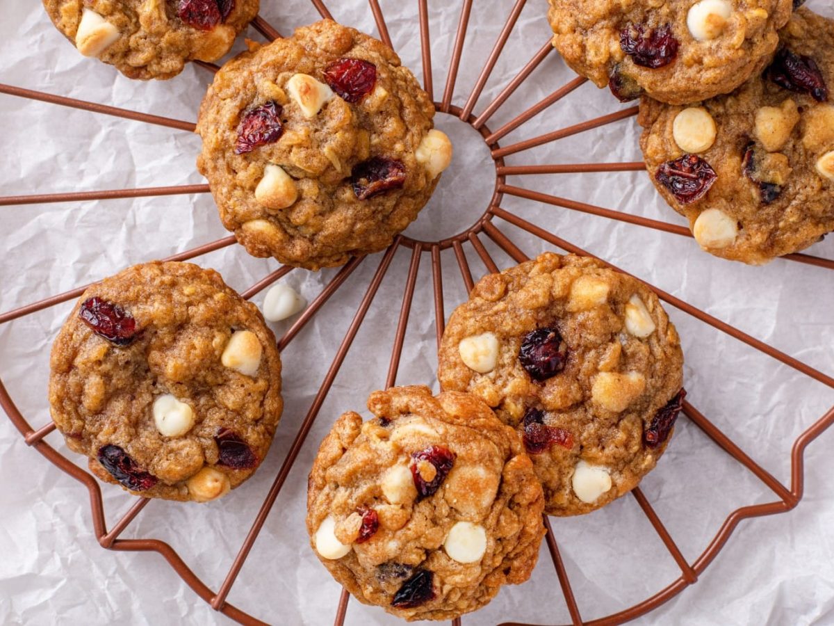 Draufsicht: Weiße-Schokolade-Cranberry-Cookies auf einem Gitter, darunter weißes Backpapier auf hellem Untergrund.