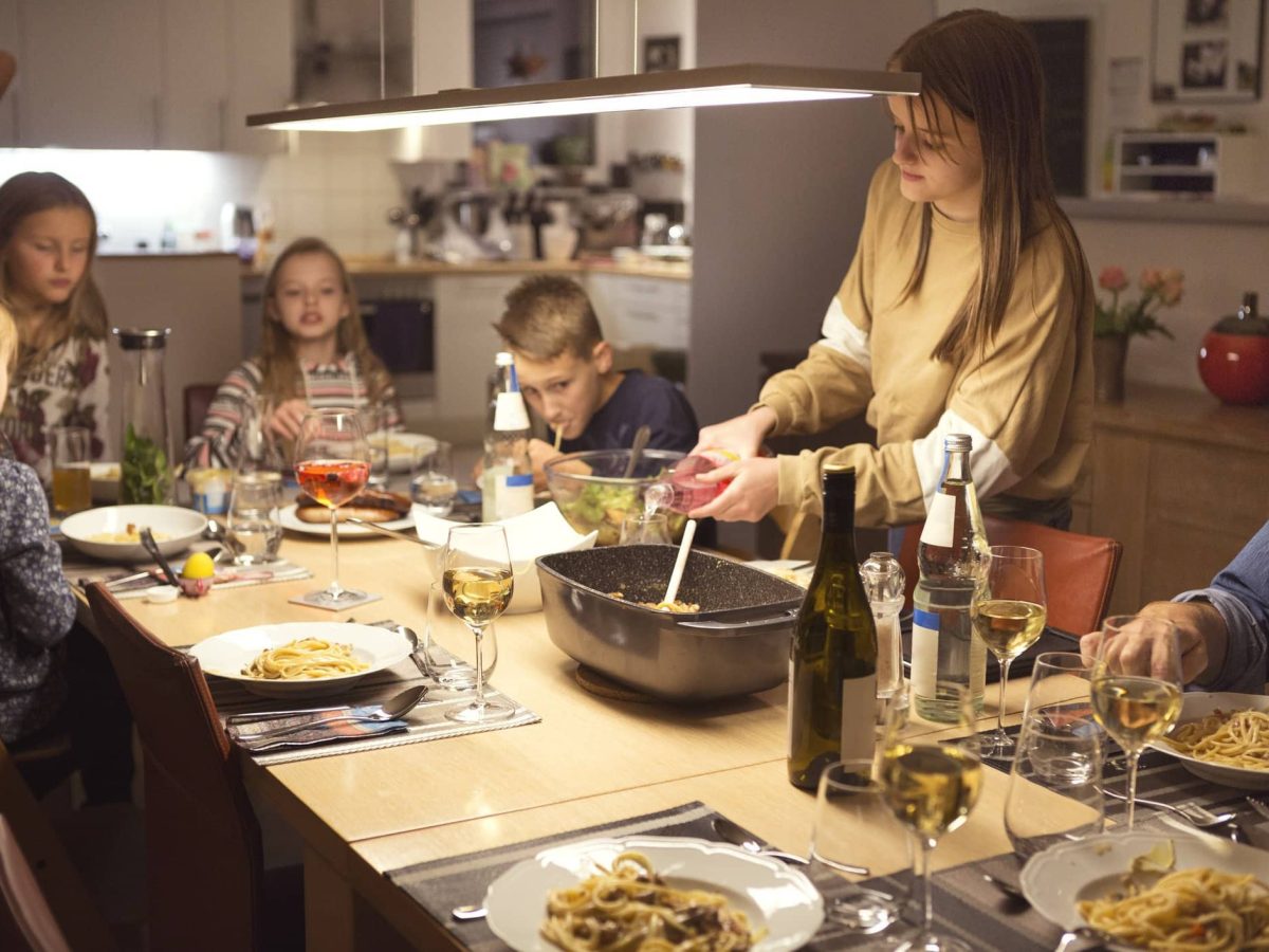 Eine Familie in der Wohnküche. Auf den Tisch stehen speisen und sie essen gemeinsam. Sie haben 25 alltagstaugliche Familienrezepte.