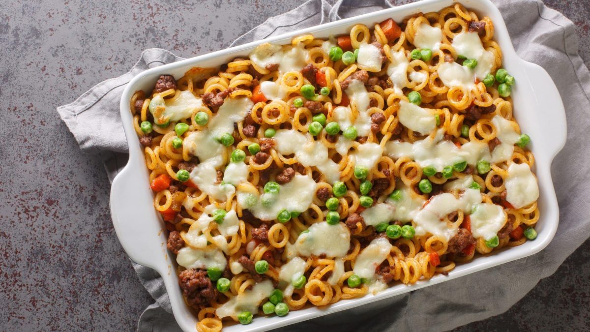 Anelletti al forno mit Erbsen und Mozzarella in weißer Auflaufform auf grauem, gesprenkeltem Tisch.