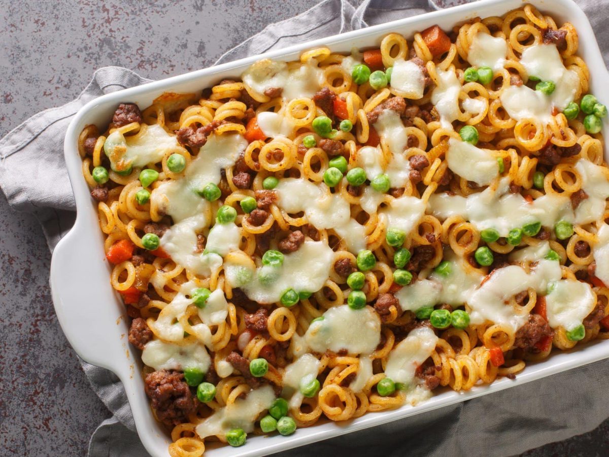 Anelletti al forno mit Erbsen und Mozzarella in weißer Auflaufform auf grauem, gesprenkeltem Tisch.