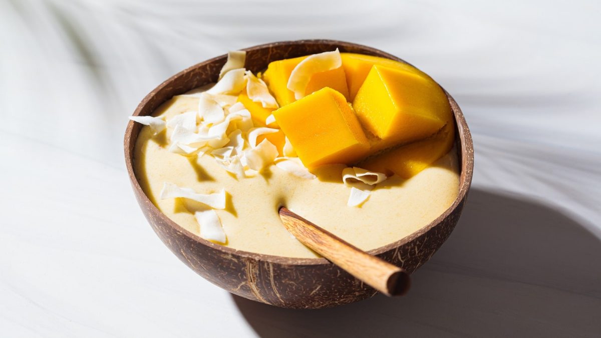 Eine Portion Ananas Smoothie Bowl in einer Holzschüssel auf einem hellen Untergrund.