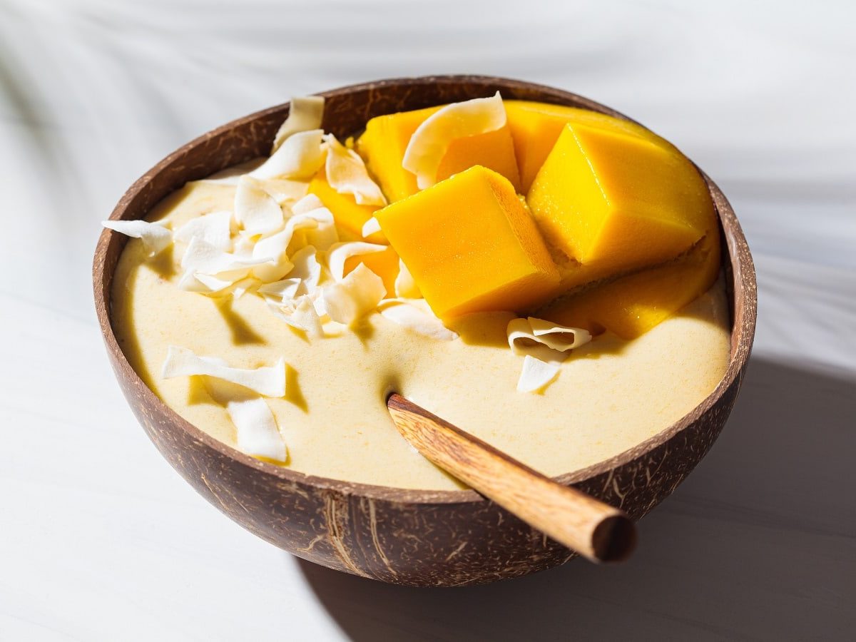 Eine Portion Ananas Smoothie Bowl in einer Holzschüssel auf einem hellen Untergrund.