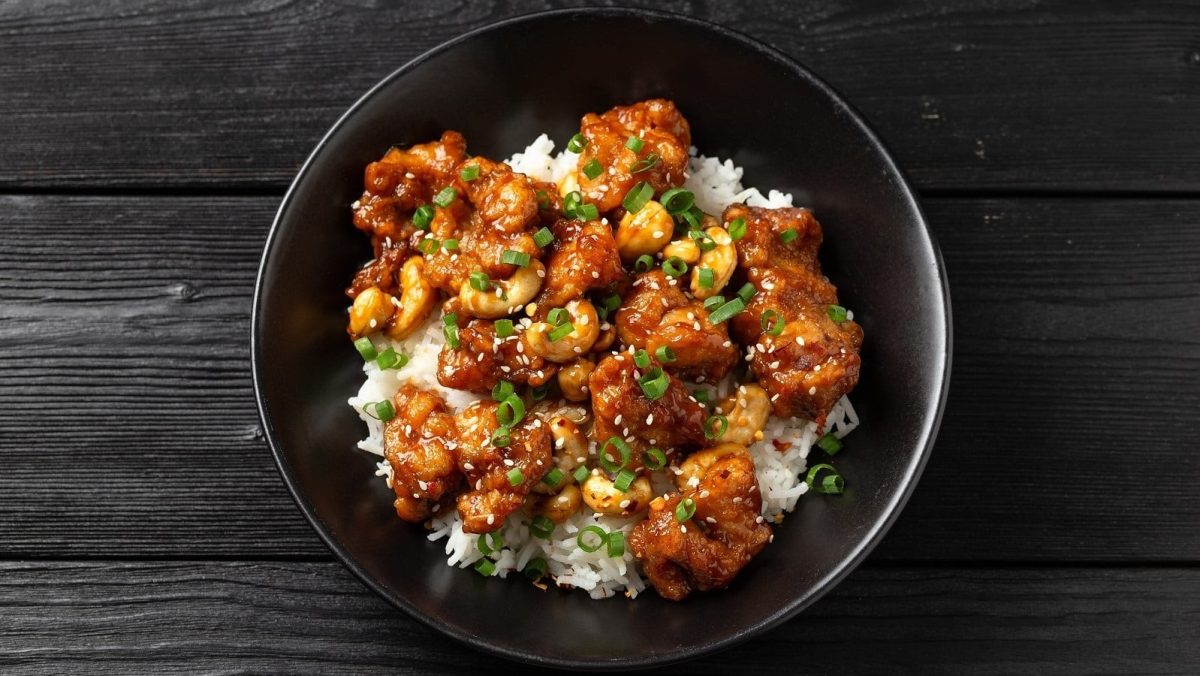 Ein dunkler Teller mit Cashew Chicken auf einem dunklen Holztisch.