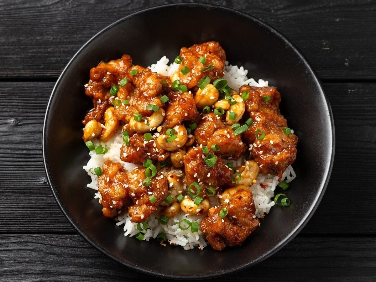 Ein dunkler Teller mit Cashew Chicken auf einem dunklen Holztisch.