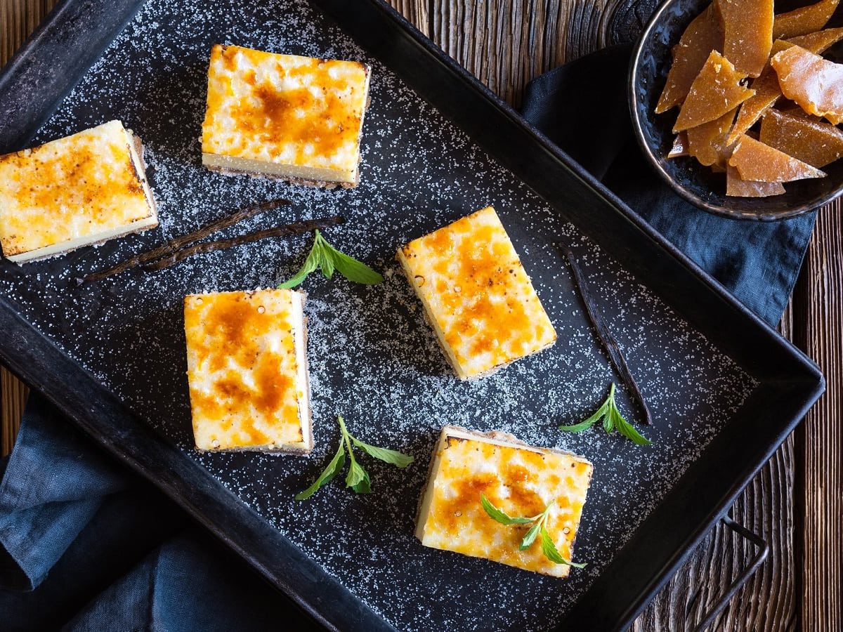 Eine schwarze Platte mit Crème Brûlée Cheesecake Bars auf einem Holztisch.