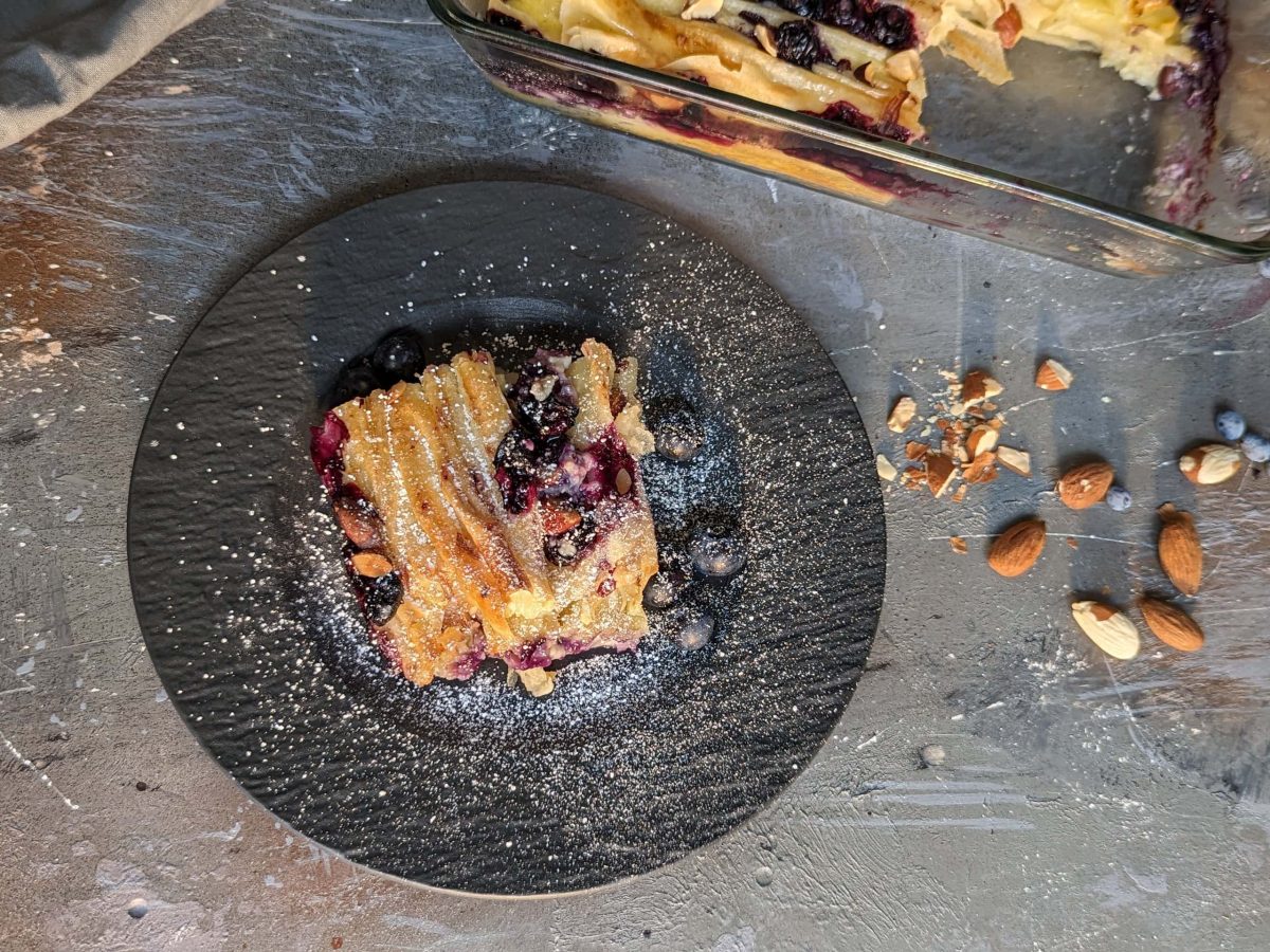 Ein schwarzer Teller mit einem Stück vom Crinkle Cake auf grauem Steinuntergrund. Daneben die Glas-Auflaufform mit dem Rest. Alles von oben fotografiert.