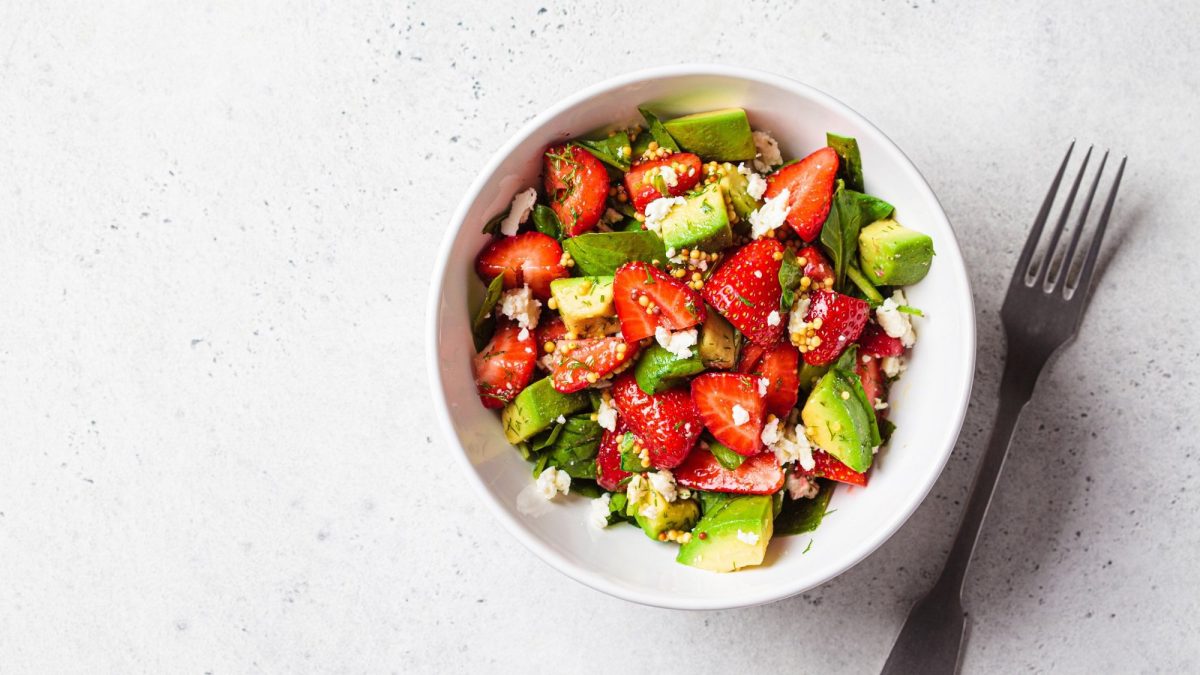 Eine Schale Erdbeer-Spinat-Salat mit Avocado & Feta in der Draufsicht auf hellem Untergrund, daneben eine Gabel.