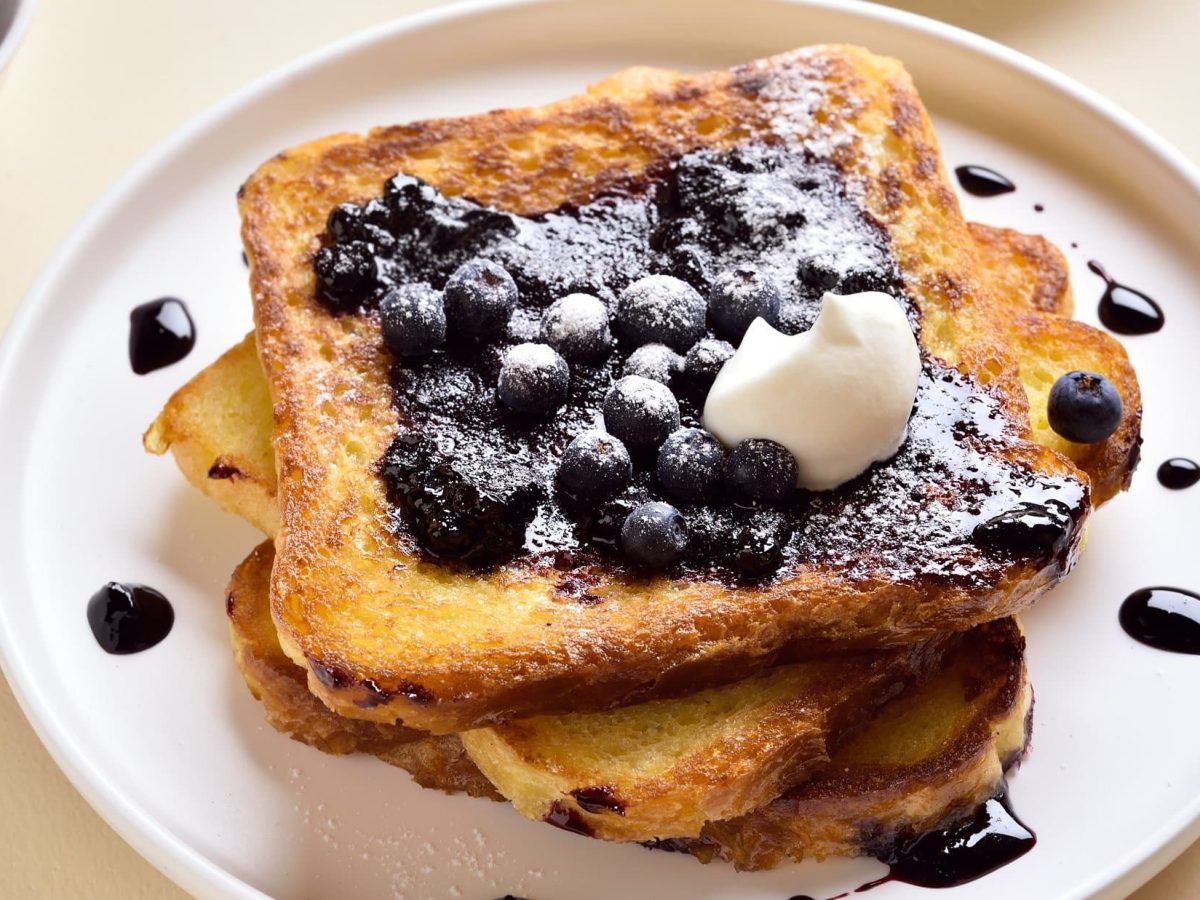 Draufsicht: ein weißer Teller mit einem French Toast mit Heidelbeeren und einem Klecks Sahne.