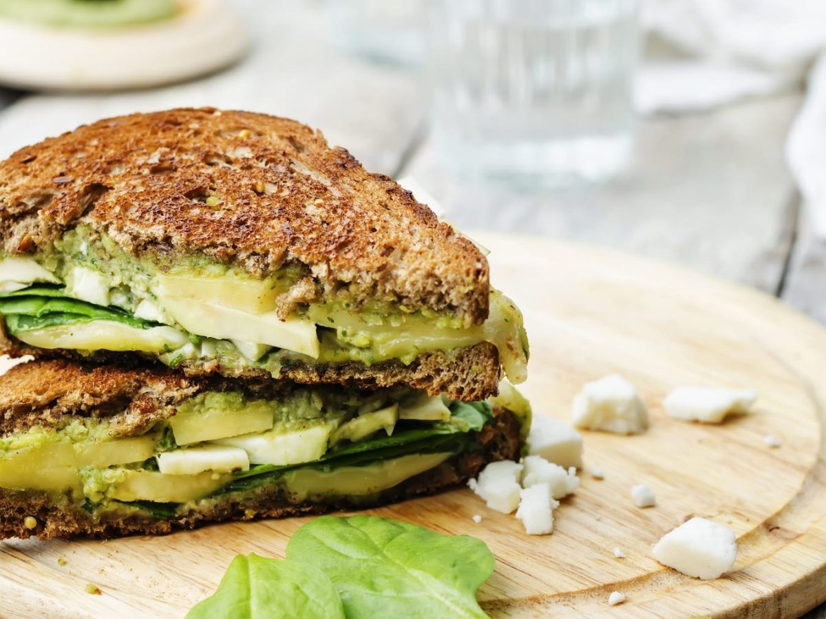 Das gegrillte Sandwich auf einem runden Holzbrett. Im Hintergrund graue Tischdecke.