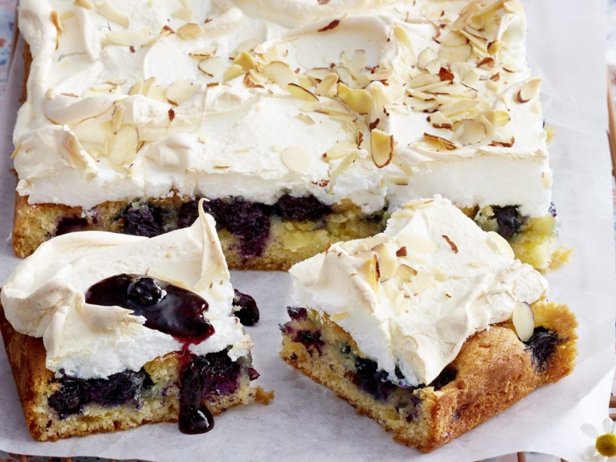 Angeschnittener Heidelbeer-Baiserkuchen auf hellem Untergrund.