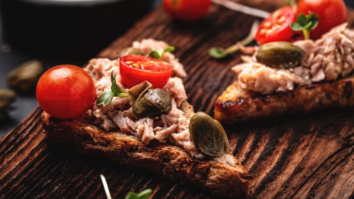 Geröstetes Knoblauch-Sandwich mit Thunfisch, Kapern und Tomaten auf Holzbrett mit Kressen. Im Bild Kapern. Draufsicht.