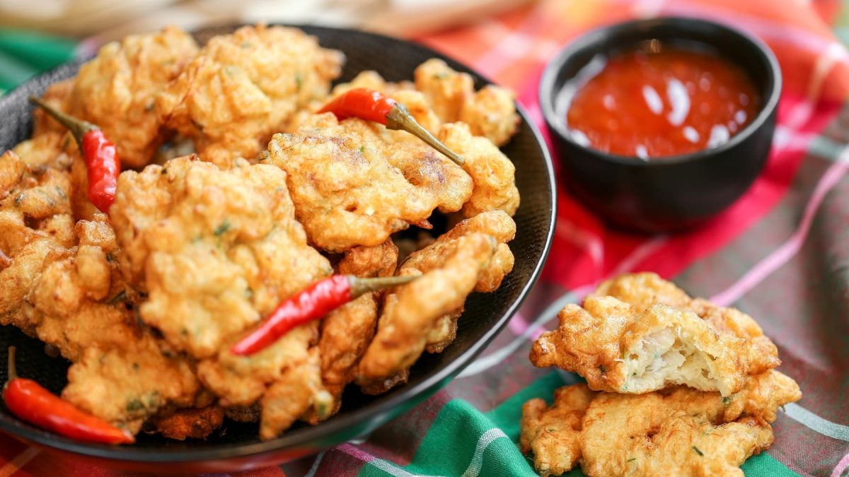 Mehrere frittierte Fischbällchen in dunklem tiefen Teller auf einer bunten Tischdecke.