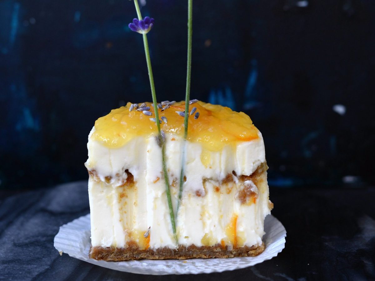 Ein angeschnittenes Lavendel-Frischkäse-Törtchen, in dem zwei Lavendelzweige stecken, Hintergrund sehr dunkel.