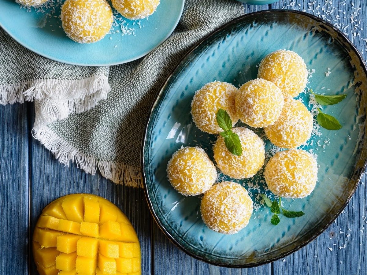 Zwei Portionen Mango Ladoo auf einem ovalen Teller auf einem blauen Holztisch.