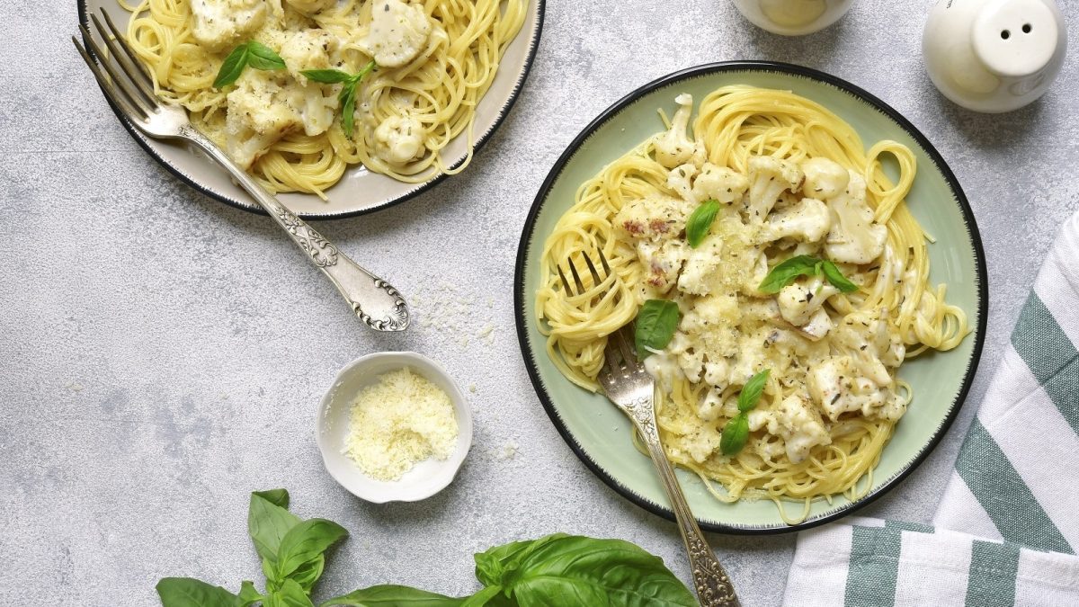 Zwei Pastateller mit Blumenkohl-Pasta in cremiger Sauce auf einem hellen Tisch.