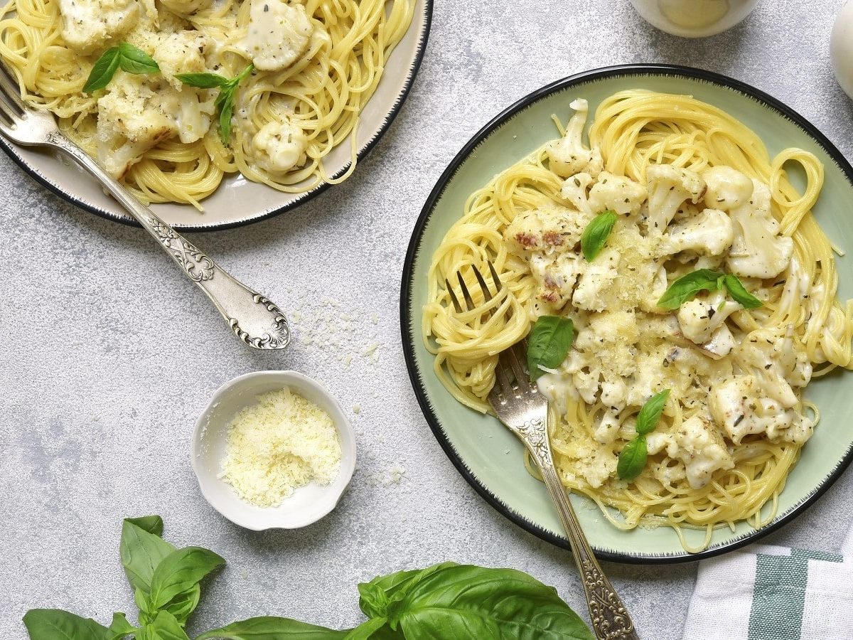 Zwei Pastateller mit Blumenkohl-Pasta in cremiger Sauce auf einem hellen Tisch.